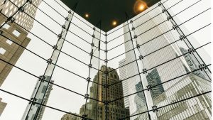 Upward view of tall city buildings reflected through a glass atrium.
